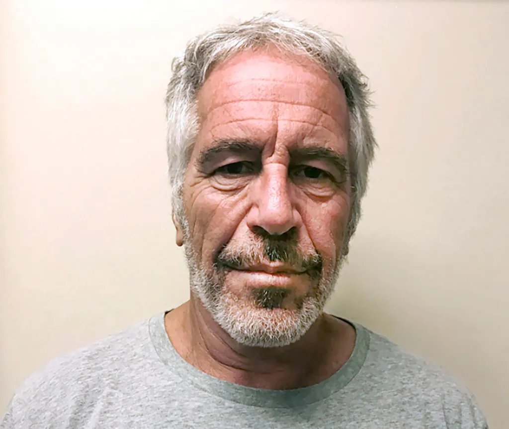 Mugshot of Jeffrey Epstein with short gray hair and a gray beard, wearing a gray t-shirt.