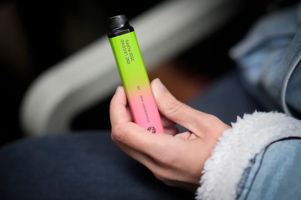 A woman holding a green and pink vape device labeled "Strawberry Kiwi".