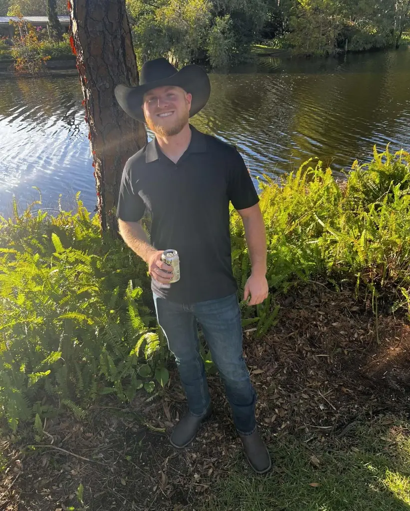 Chance Allison in a black cowboy hat, black shirt, and jeans, holding a can, standing by a body of water.