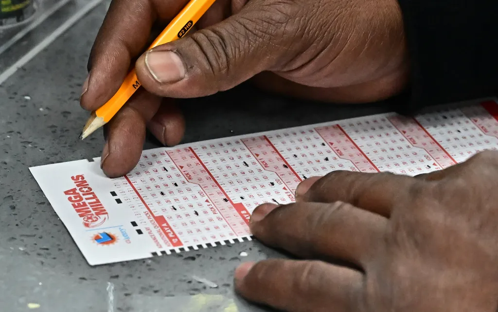 A person fills out a Mega Millions lottery ticket with a pencil.