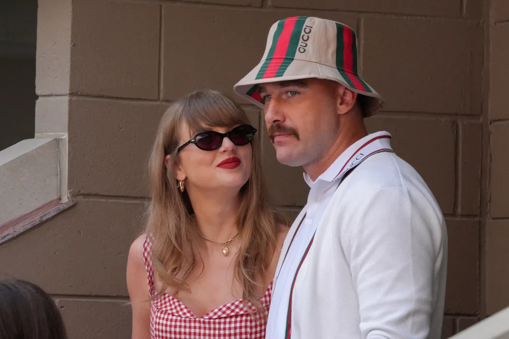 Taylor Swift in a red gingham dress and sunglasses, with Travis Kelce in a Gucci bucket hat and white cardigan.