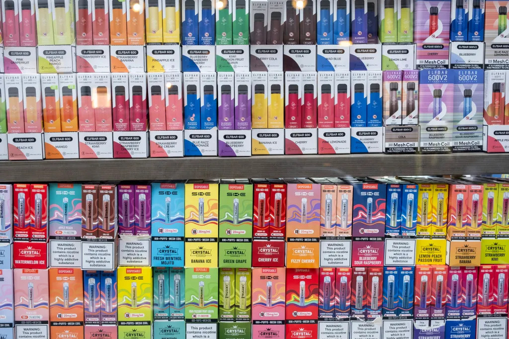 A display of various colorful disposable vapes from brands like Elfbar and SKE, with flavors such as pineapple peach mango, strawberry ice, cherry, and watermelon ice.