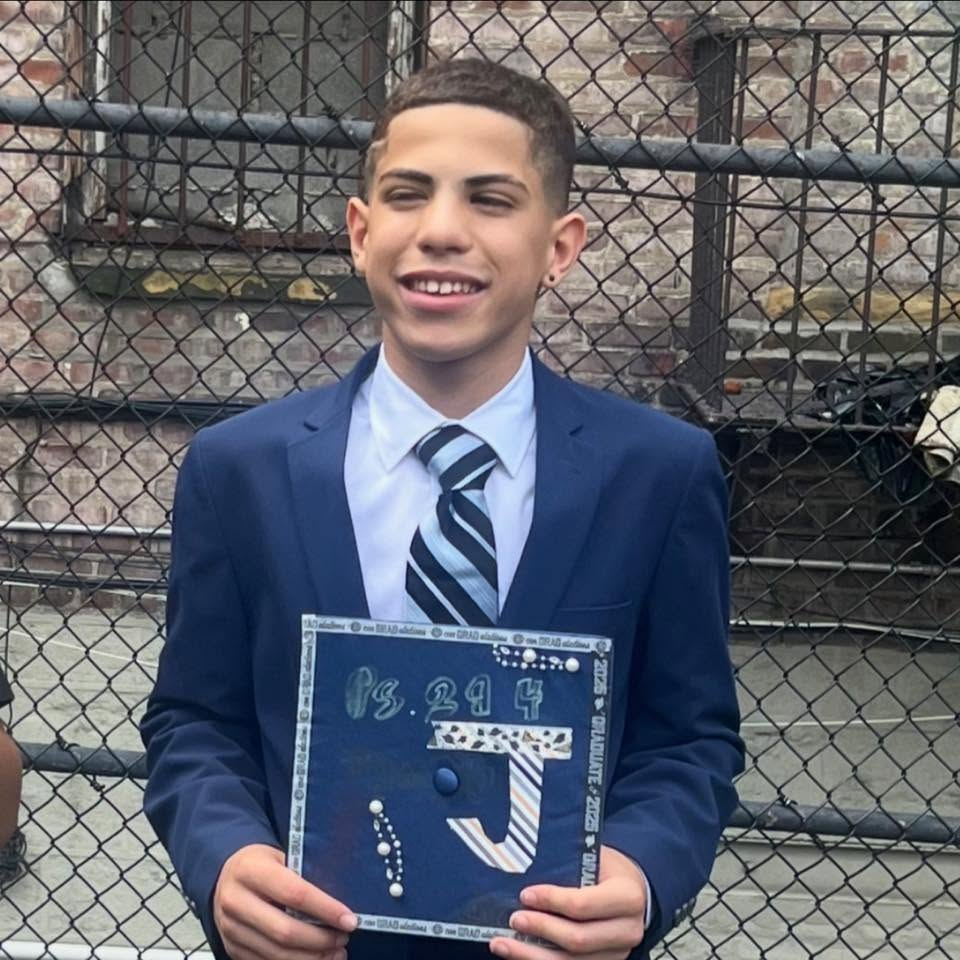 Jacob Freytes, 12, smiling and holding a decorated graduation cap.