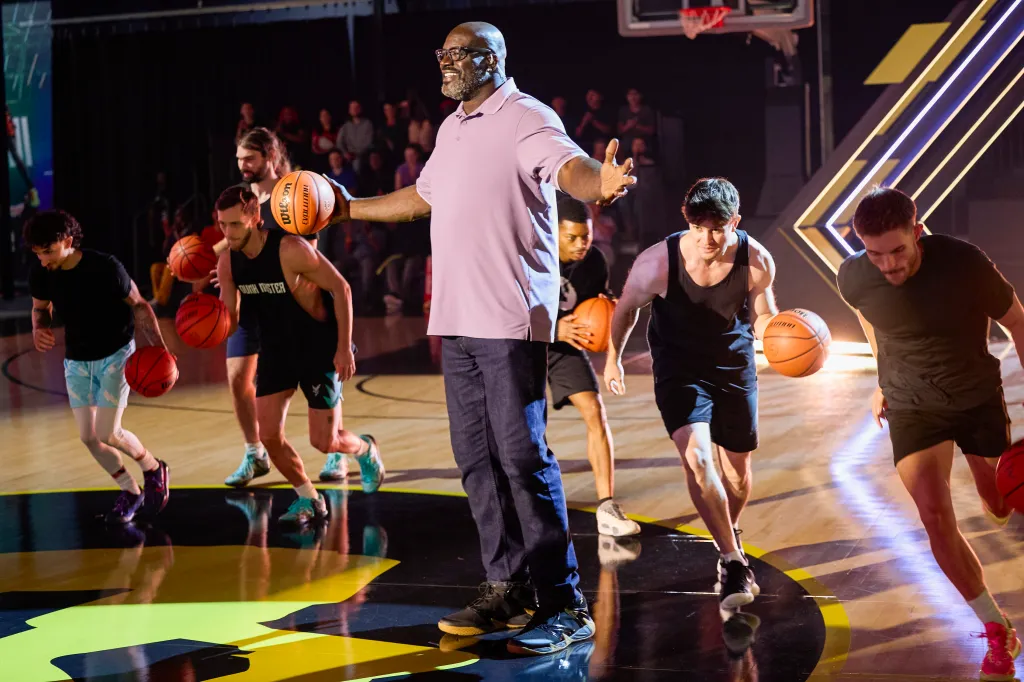 Shaquille O'Neal stands with a basketball on a court surrounded by other players.