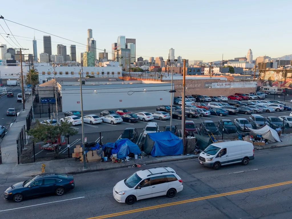 Homeless encampments line a street in Downtown Los Angeles with a city skyline in the background.
