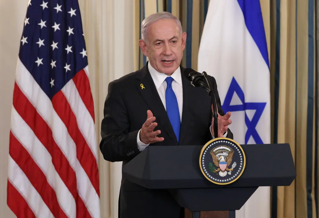 Benjamin Netanyahu speaking at a podium with US and Israeli flags behind him.