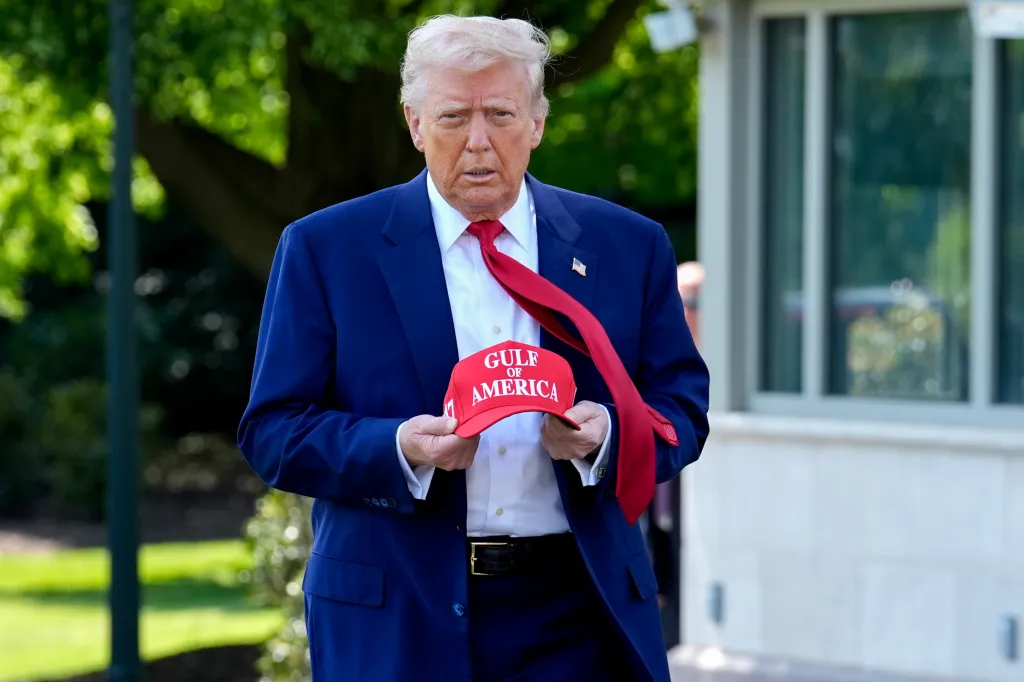 Donald Trump holds a red baseball cap with "GULF OF AMERICA" written on it.
