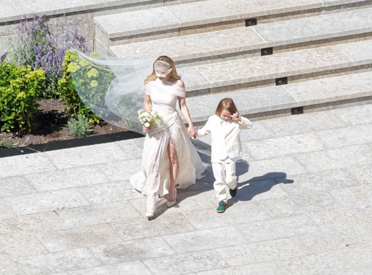 Emma Roberts in a wedding gown holding hands with a child in a white suit.
