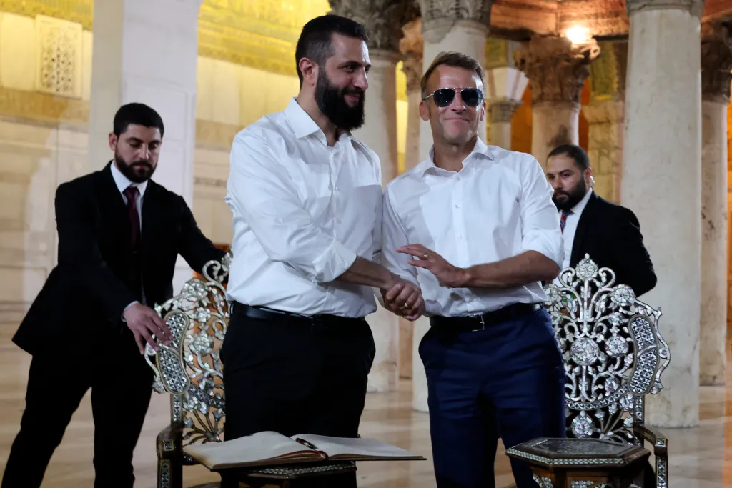 French President Emmanuel Macron (R) shakes hands with Syrian President Ahmed Al-Charaa during a visit to the Umayyad Mosque.