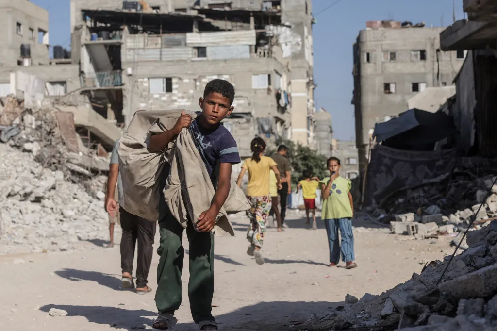 A Palestinian boy carries a bag over his shoulder as he walks through a heavily damaged street in Khan Yunis.
