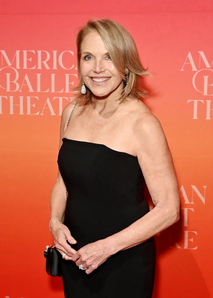 Katie Couric in a black dress with diamond earrings and bracelet, holding a clutch, smiling at the 2026 American Ballet Theatre Spring Gala.