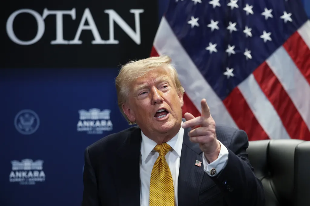 US President Donald Trump speaks at the NATO Summit in Ankara, with a US flag and "OTAN" visible in the background.