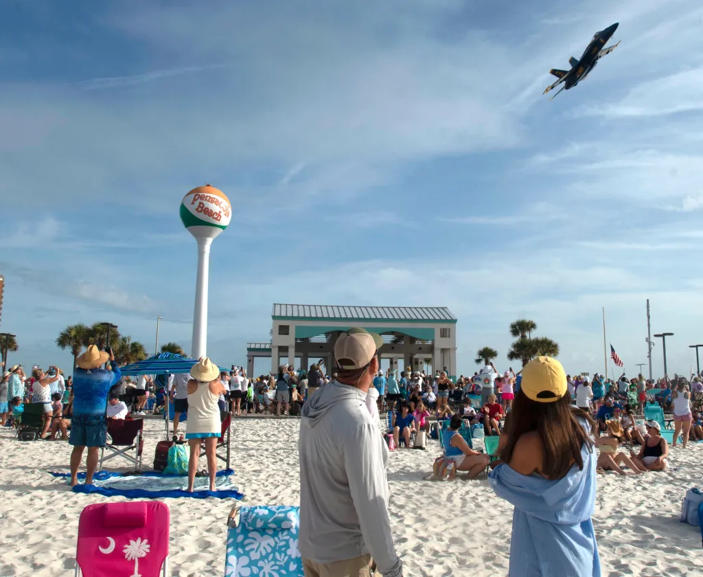 Spectators watching a Blue Angels jet fly by the Pensacola Beach water tower.