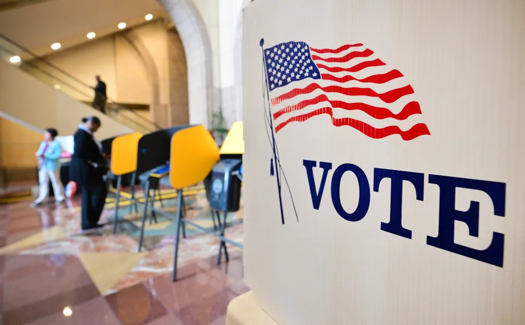 A white ballot box with an American flag and the word "VOTE" in blue letters.