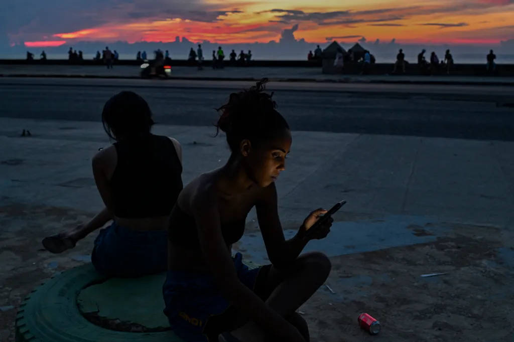 A woman looks at a phone while sitting on the side of the road during a blackout on July 6, 2026.