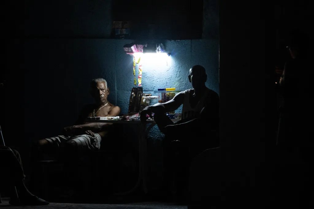 Two men sit around a table illuminated by a single light during a power outage.