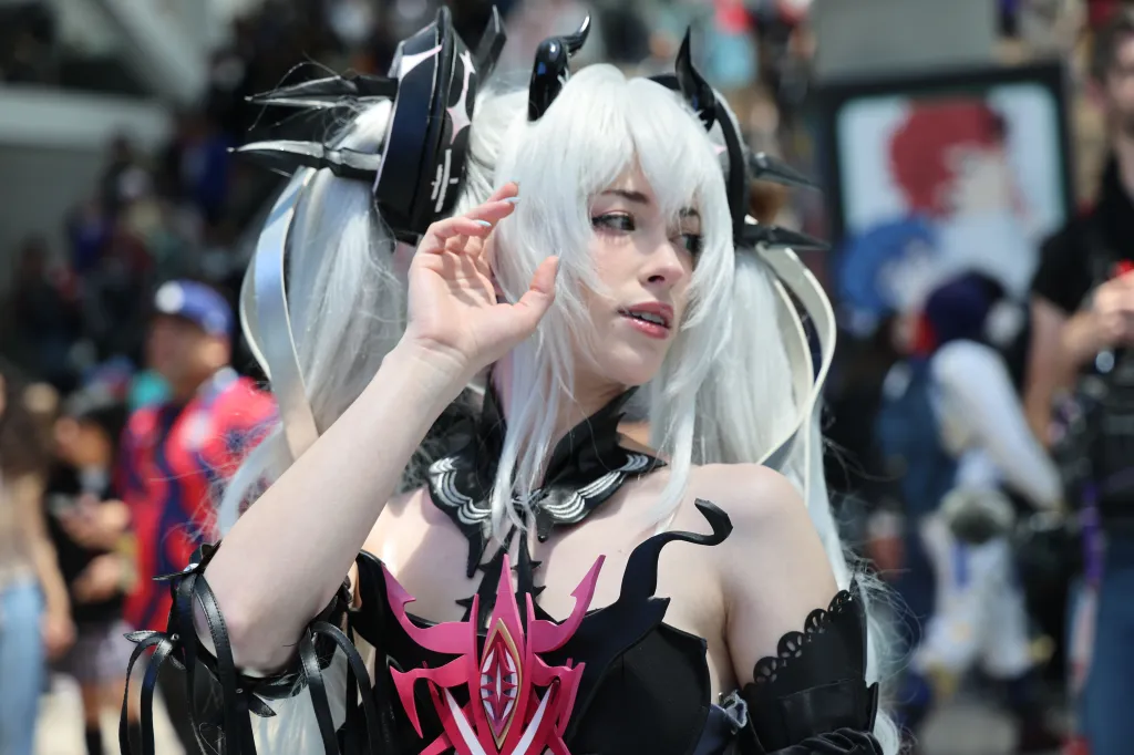 An anime fan dressed in a costume with white hair, black horns, and a black and pink outfit at Anime Expo.