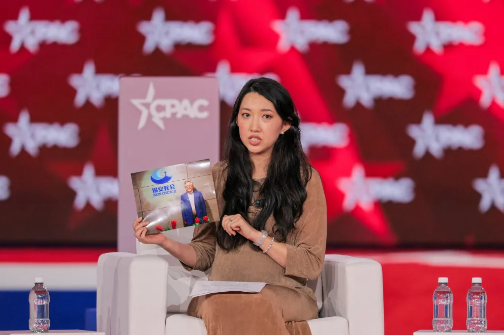 Grace Jin Drexel holding a photo of Pastor Ezra Jin with Zion Church logo on stage at CPAC.