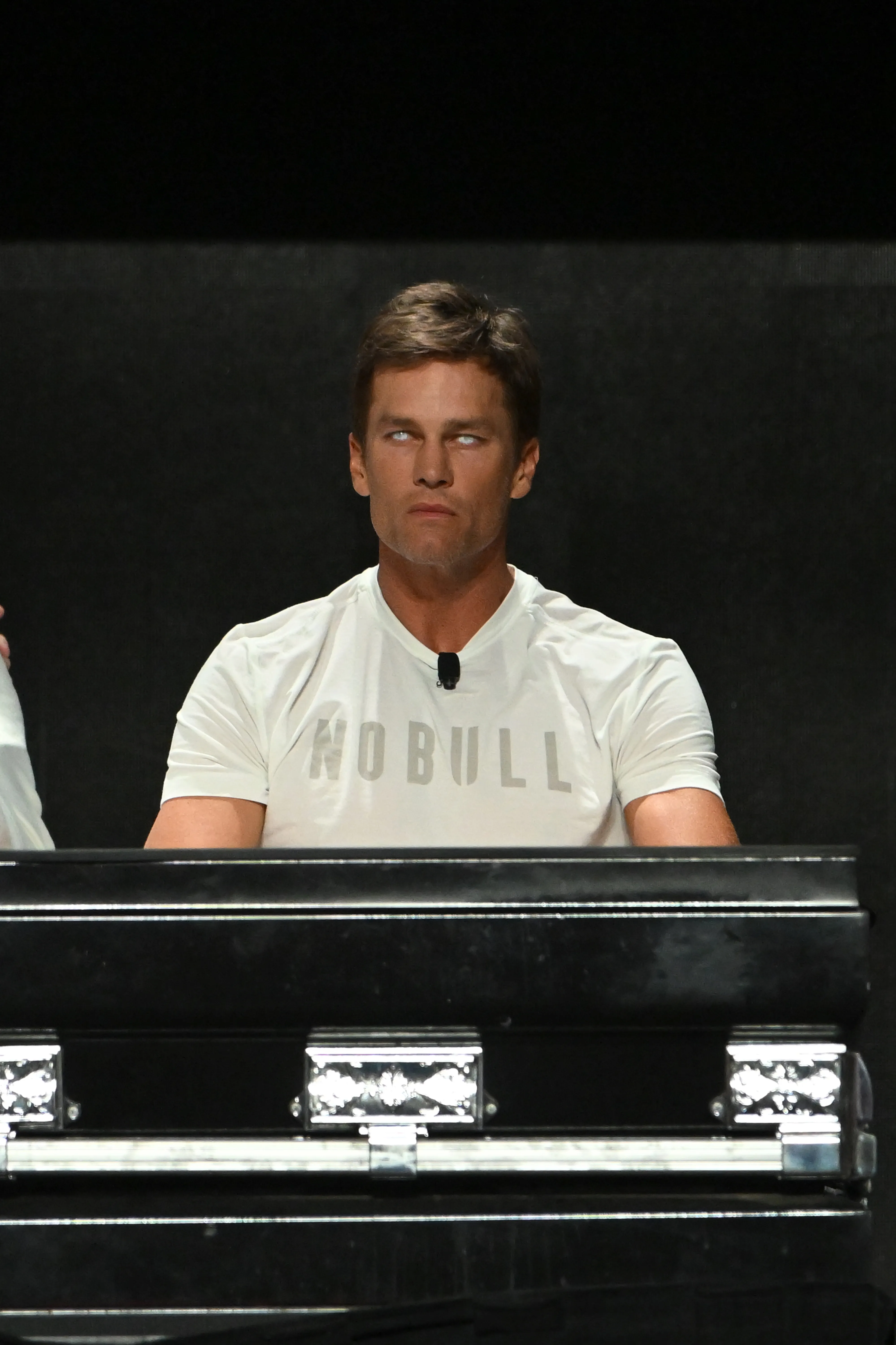 Tom Brady, with his eyes rolled back, wears a white t-shirt with "NOBULL" printed on it.