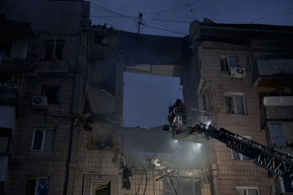 A rescuer in a raised crane bucket works on a severely damaged multi-story residential building after a missile strike in Kyiv, Ukraine.