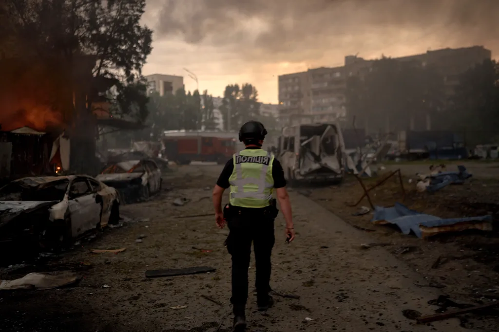 A police officer walks through a smoke-filled, debris-strewn street past burning and destroyed vehicles and buildings in Kyiv after a Russian missile strike.