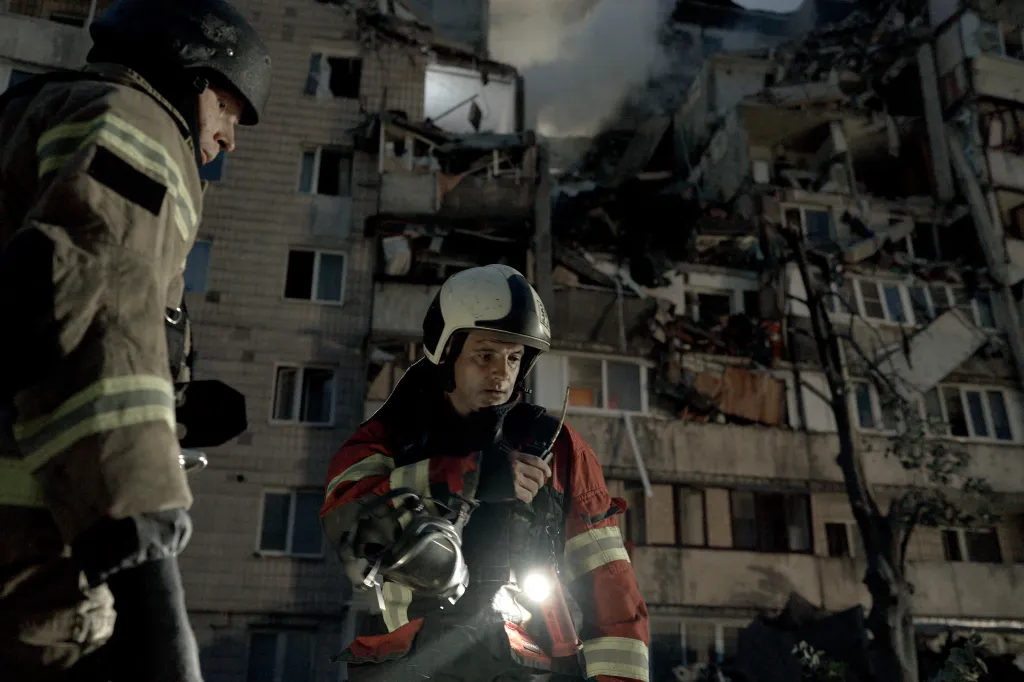 Rescuers in helmets and protective gear work at night in front of a heavily damaged residential building following a Russian missile strike in Kyiv, Ukraine.