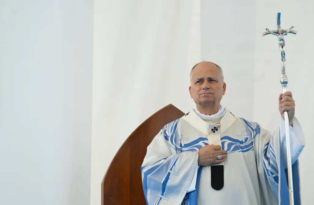 Pope Leo XIV, dressed in white and blue vestments, holds a silver crucifix-topped staff during his pastoral visit to Lampedusa.
