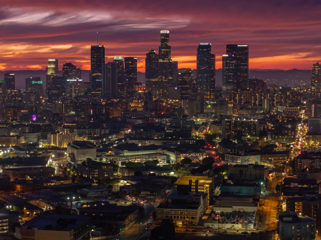 Aerial view of downtown Los Angeles at dusk with the city lights on and a vibrant red and purple sky.