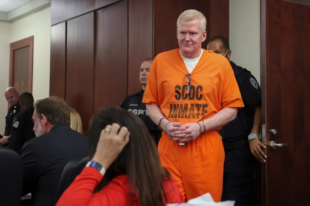 Alex Murdaugh, in an orange jumpsuit and handcuffs, stands in a judicial center.