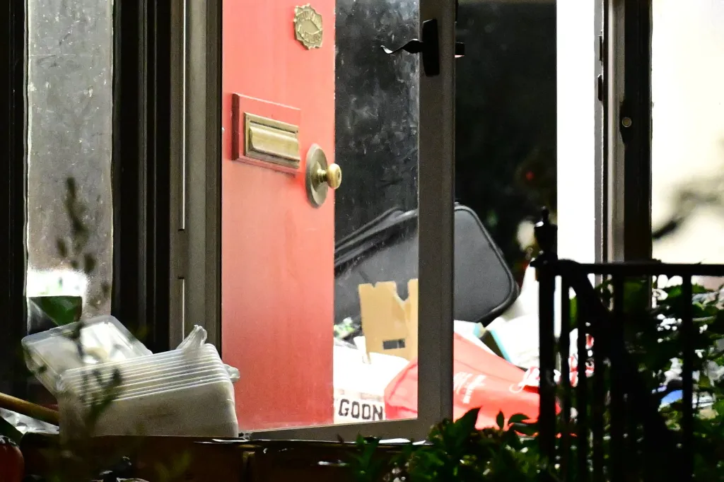 Red front door of a house with a gold knocker, golden doorknob, and an open window revealing objects inside, related to the murder of Marian Green.