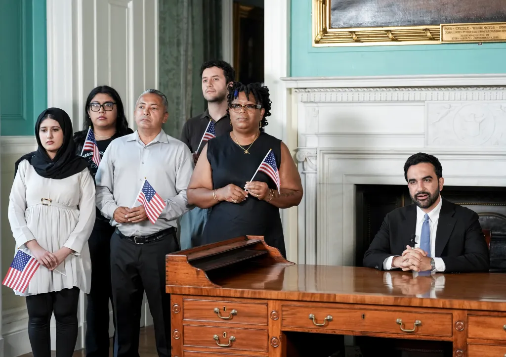 New York City Mayor Zohran Mamdani speaks from George Washington's desk surrounded by recently naturalized citizens holding American flags.
