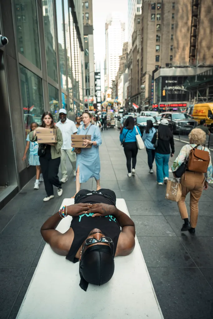 A man lying on a bench on a busy New York City sidewalk during a heat wave.