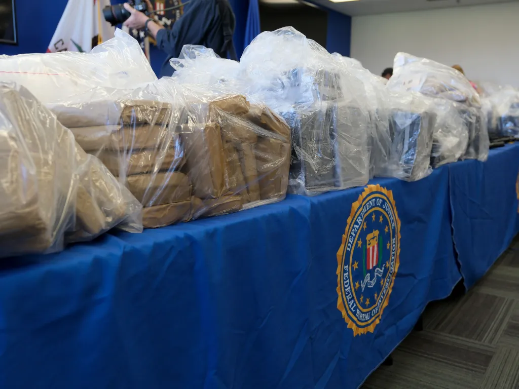 Evidence seized from an international crime syndicate, displayed in clear plastic bags on a table with a blue cloth featuring the FBI seal.