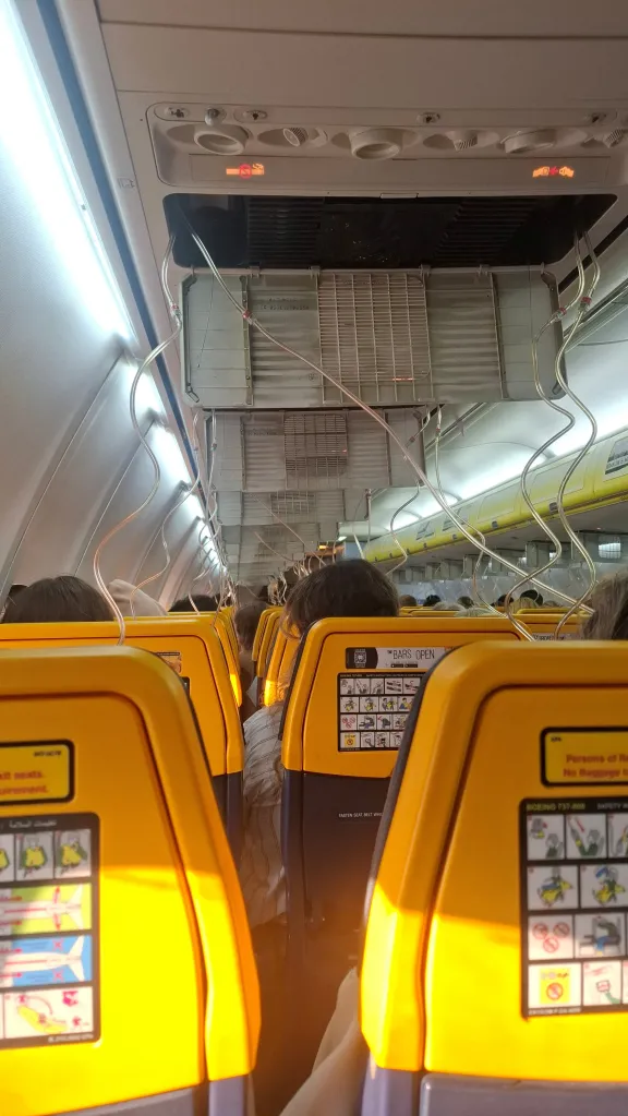 Interior of a Ryanair aircraft cabin after an emergency landing, showing deployed oxygen masks and exposed ceiling panels.