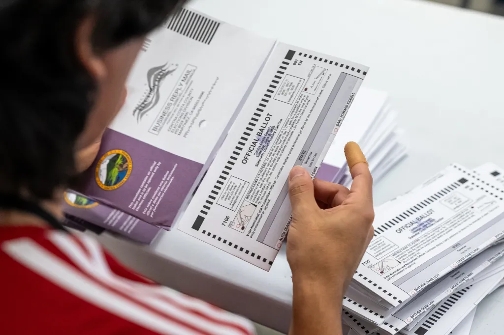An election worker extracting a mail-in ballot from an envelope.