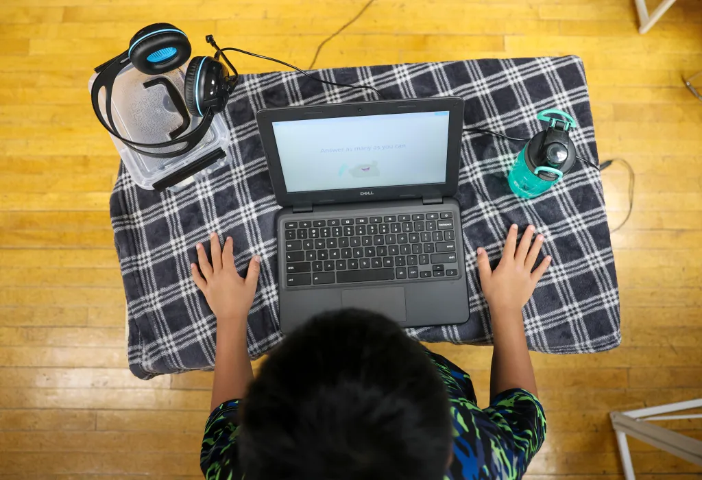 Overhead view of Lukkas Powao, 8, with his hands poised over a Dell laptop, answering problem-solving questions.