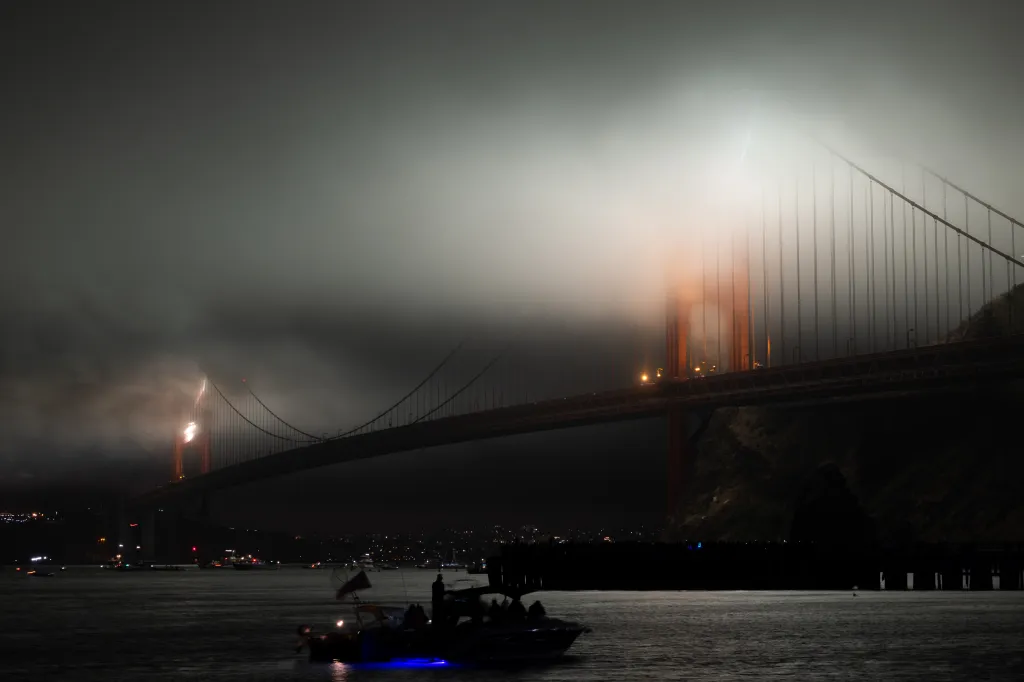Fireworks erupting from the Golden Gate Bridge, partially obscured by fog.