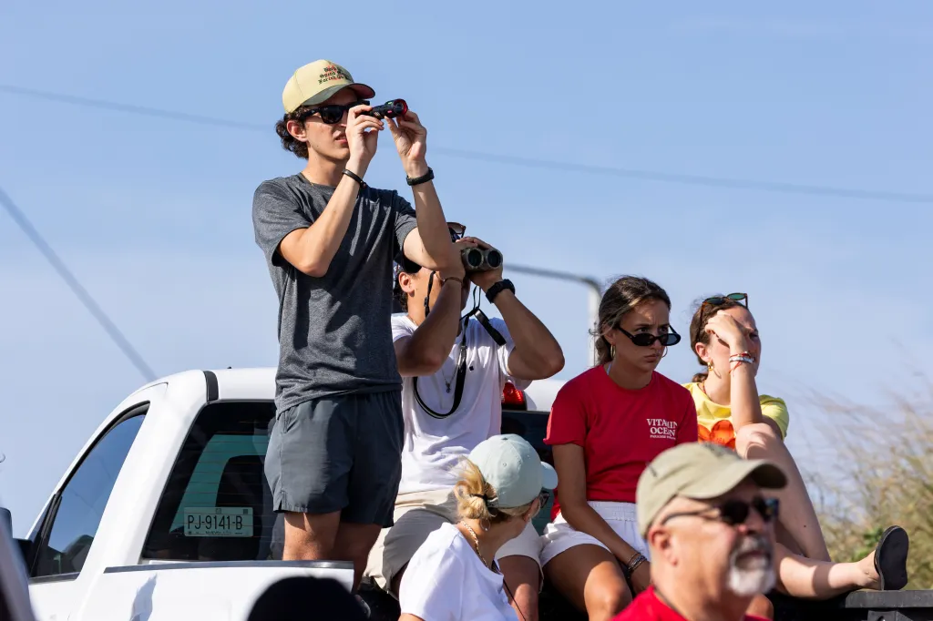 Spectators watch a planned SpaceX Starship rocket launch from the back of a white pickup truck.