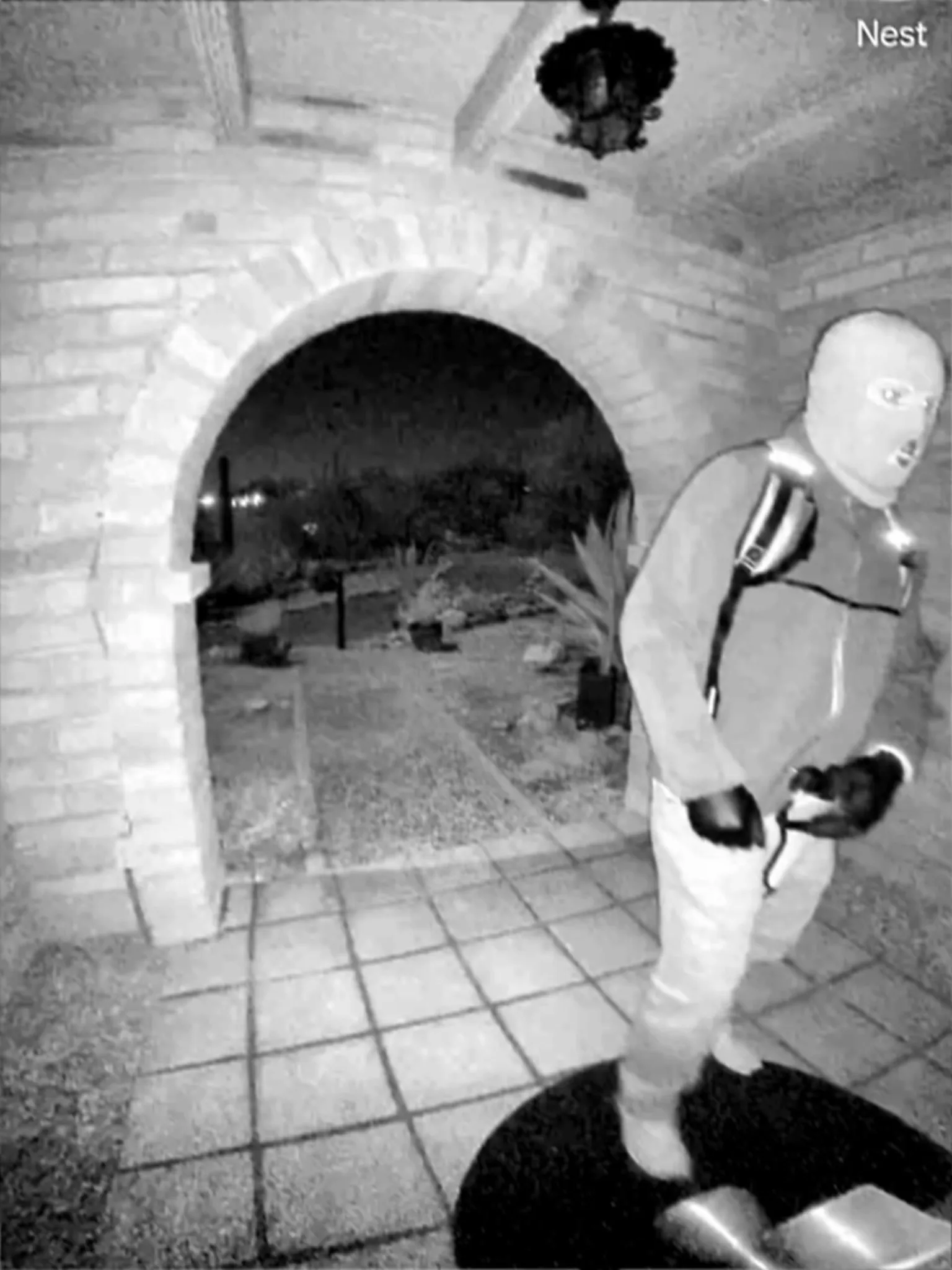 Surveillance image of a person in a ski mask and light-colored clothing.