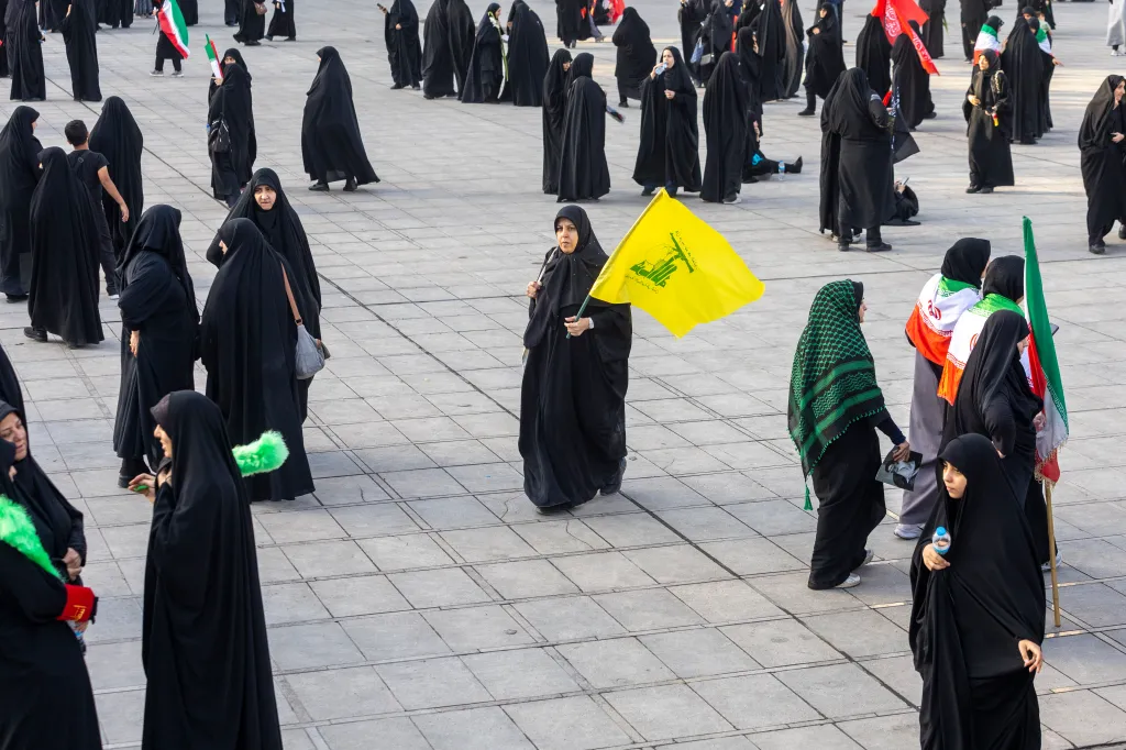 A woman in a black chador holds a yellow Hezbollah flag during a farewell ceremony in Tehran, Iran.
