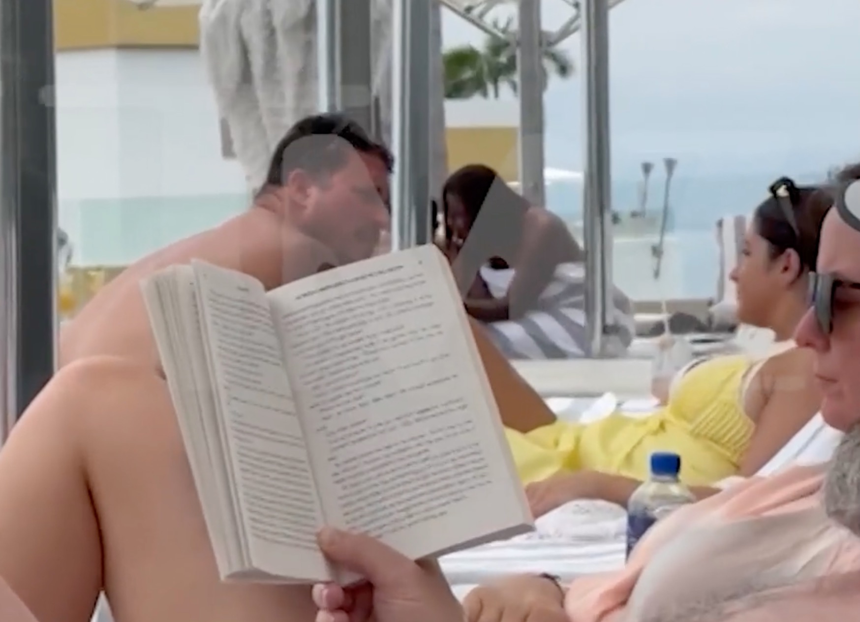 People lounging by a pool with the ocean in the background.