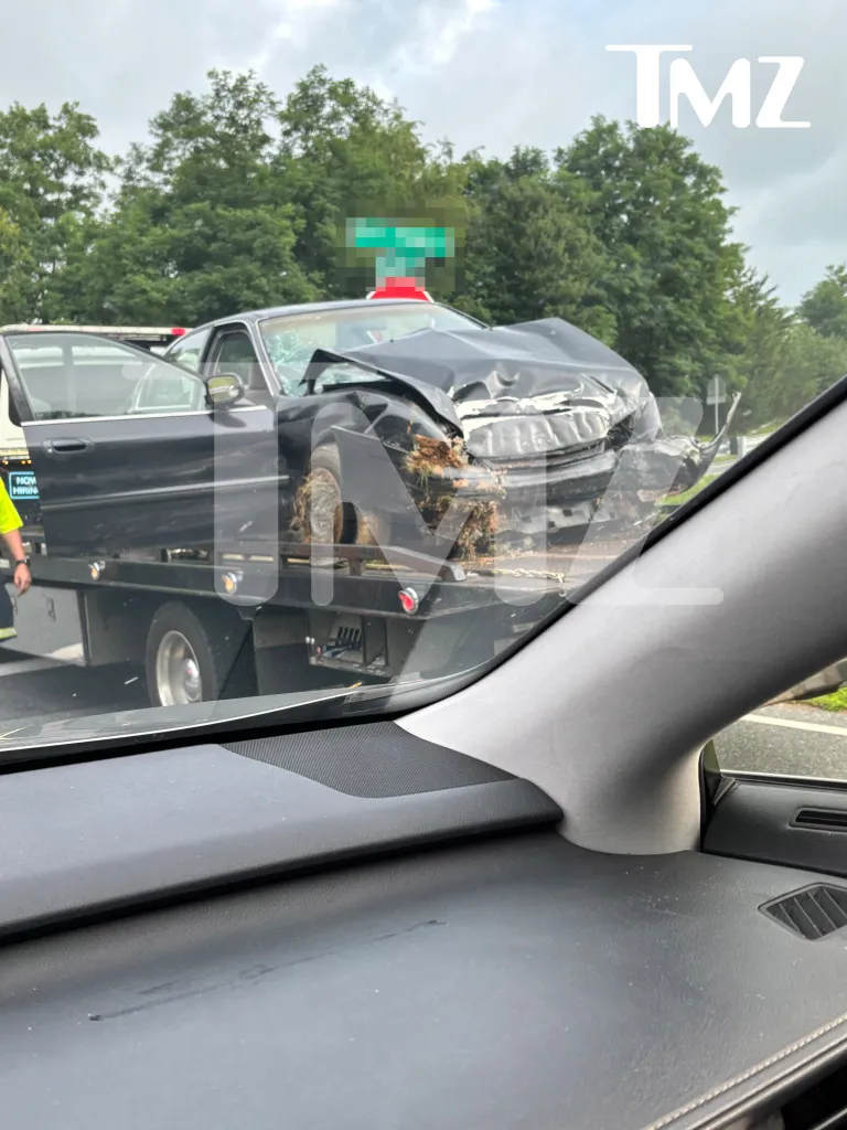 A severely damaged black car, with its front end crushed and windshield shattered, is loaded onto a tow truck.
