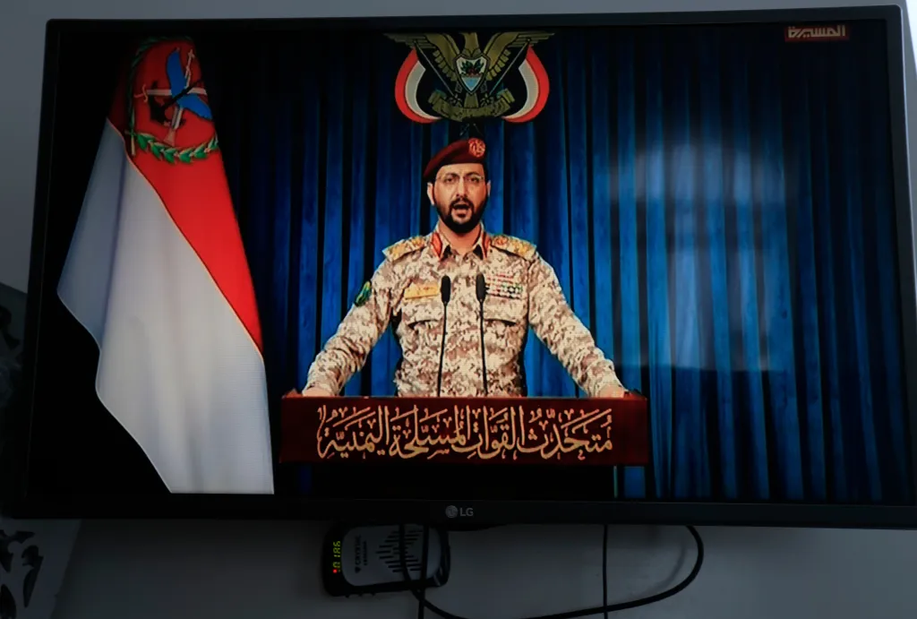 A man in military uniform speaking at a podium on a television screen.