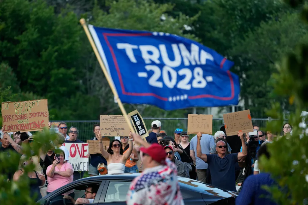A counter-protester waves a Trump 2028 flag while anti-ICE demonstrators hold signs in Biddeford, Maine.