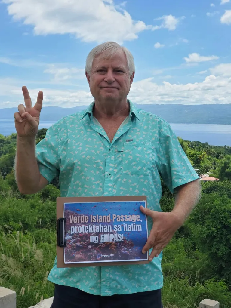 Kent Carpenter holding a sign that reads "Verde Island Passage, protektahan sa ilalim ng ENIPAS!" and making a peace sign.