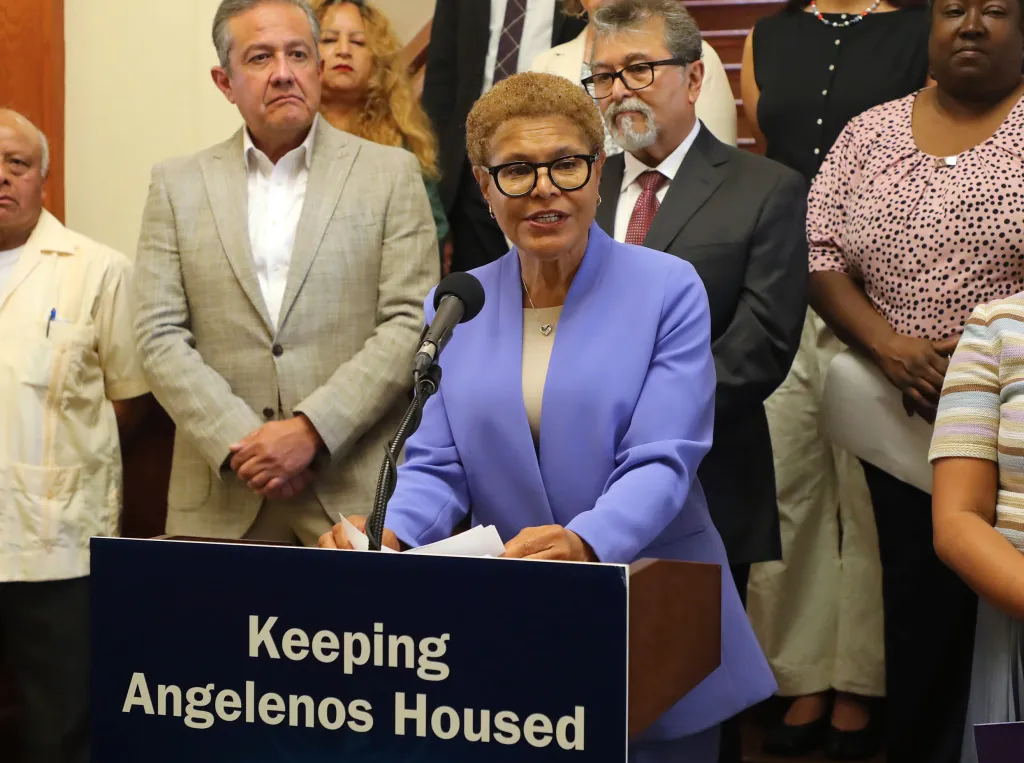 Karen Bass speaks at a podium with the text "Keeping Angelenos Housed" on it, announcing affordable housing funding.