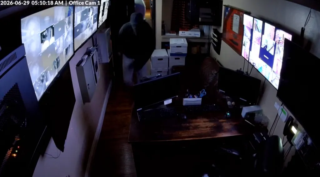 Security footage shows a hooded thief moving past multiple security monitors.