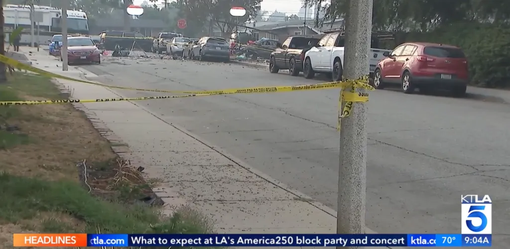 Street blocked off by yellow police tape with debris scattered on the ground and damaged cars in the background.