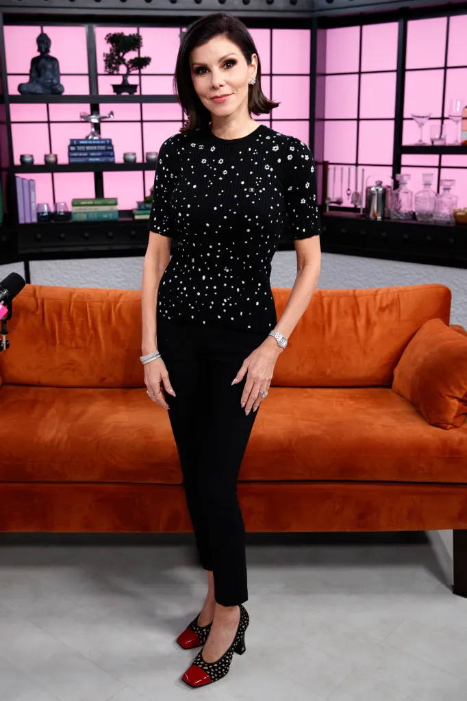 Heather Dubrow standing in front of an orange couch and a pink-lit wall.