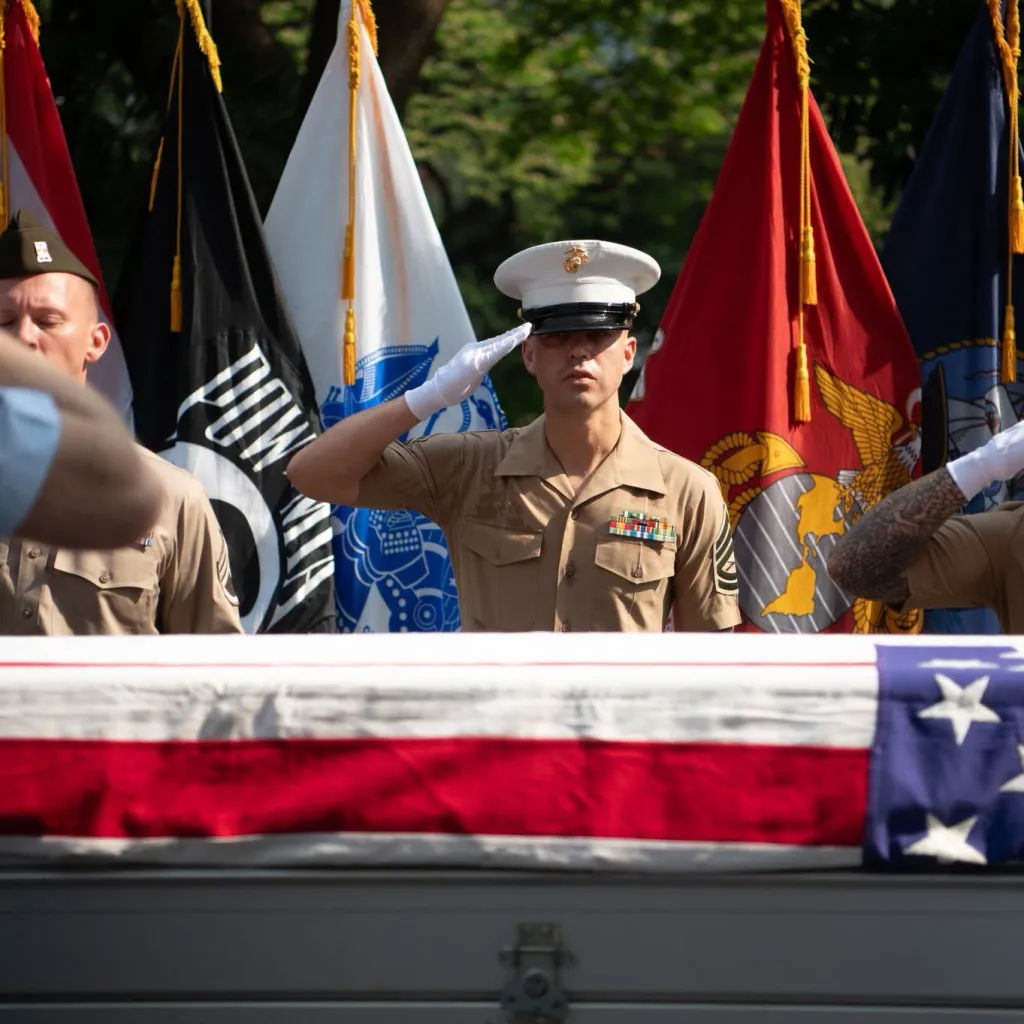 Marine in uniform saluting a flag-draped coffin.